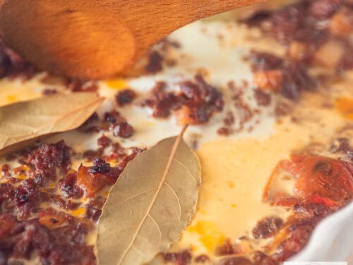 Een vierkante foto met een bobotie ovenschotel met gehakt, laurier, ei, appel en rozijnen.