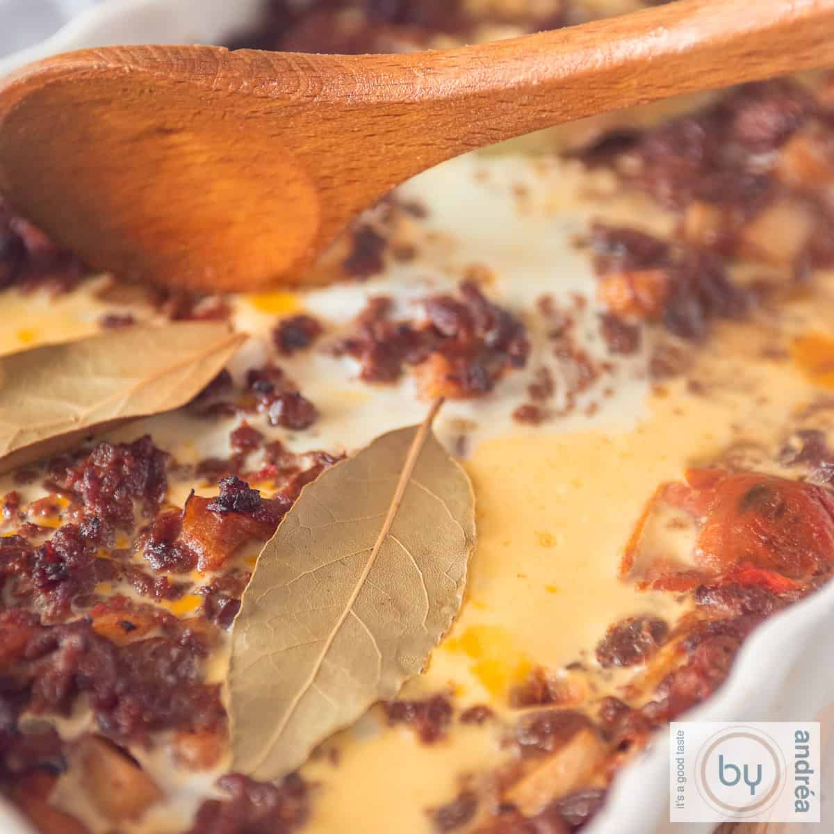 Een vierkante foto met een bobotie ovenschotel met gehakt, laurier, ei, appel en rozijnen.