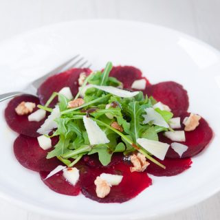 Carpaccio van bieten op een bord, met kaas, rucola, peer en walnoten