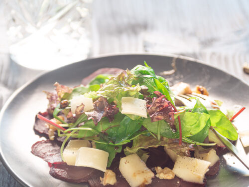 Carpaccio van bieten op een bord, met kaas, rucola, peer en walnoten