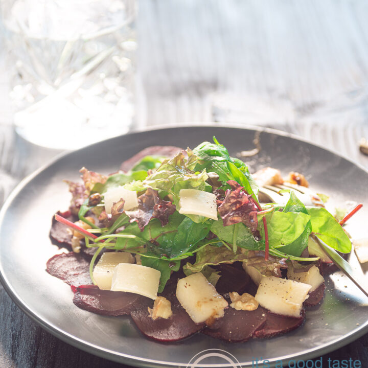 Carpaccio van bieten op een bord, met kaas, rucola, peer en walnoten