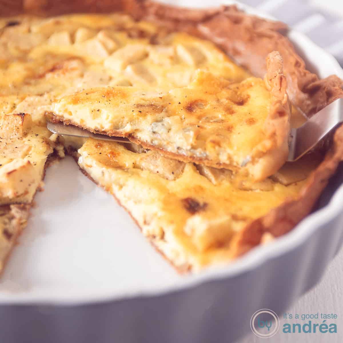 Een vierkante foto met een gorgonzola quiche met appel. Een punt eruit gesneden, die ligt er bovenop.