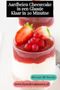 Een glas gevuld met laagjes koek, romige yoghurt roomkaas vulling jam en vers rood fruit. Een tekst: Aardbeien cheesecake in een glaasje, klaar in 20 minuten