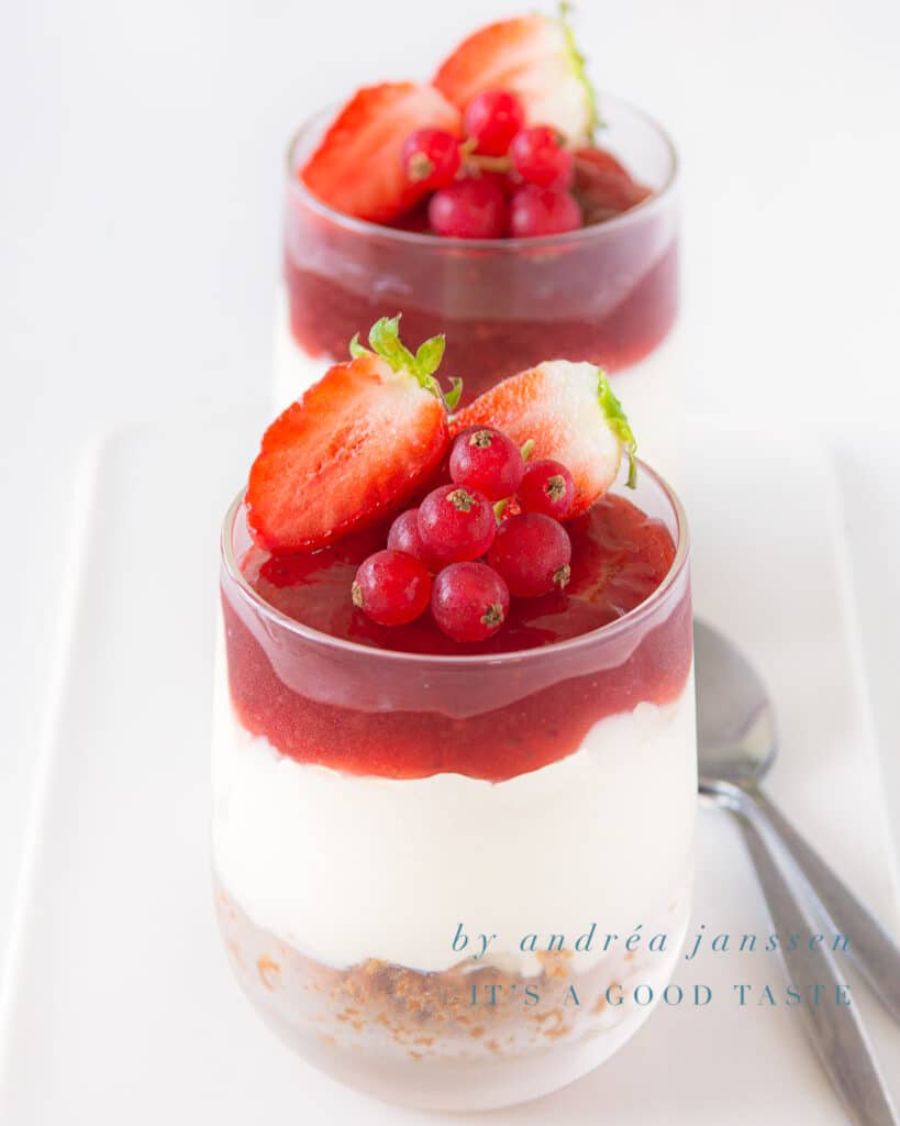 Twee glaasjes met aardbeien cheesecake. Aan de rechterzijde liggen twee lepels