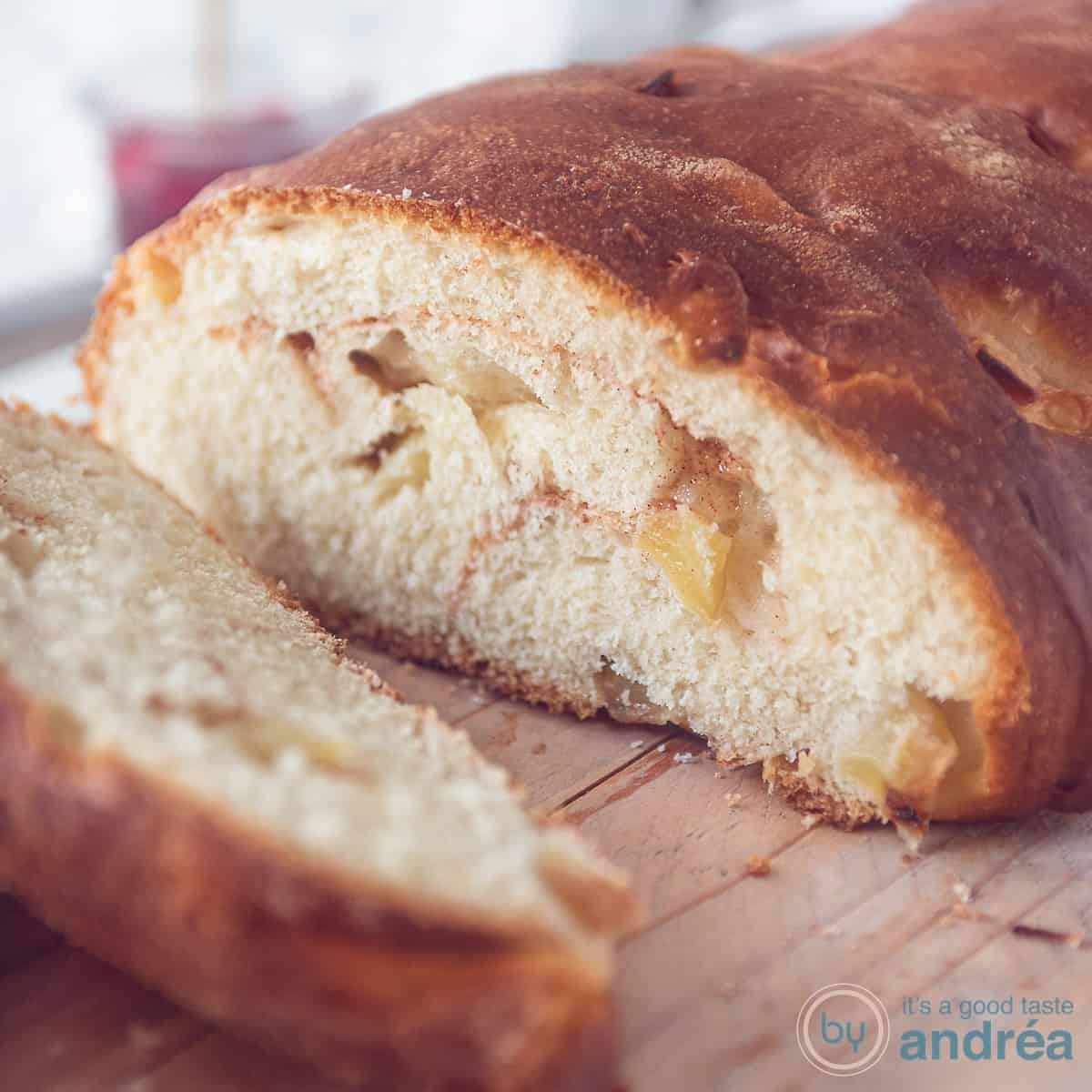 Een vierkante foto met een houten plank met daarop een appelbrood. Een plakje erafgesneden