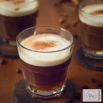 Een vierkante foto met een bruine tafel met drie kopjes met apfelkorn honing café au lait ingeschonken.