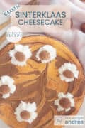 Een cheesecake met een swirl van speculoos, gegarneerd met slagroom en pepernoten. Bovenin een tekst: Sinterklaas cheesecake, makkelijk recept, bakken