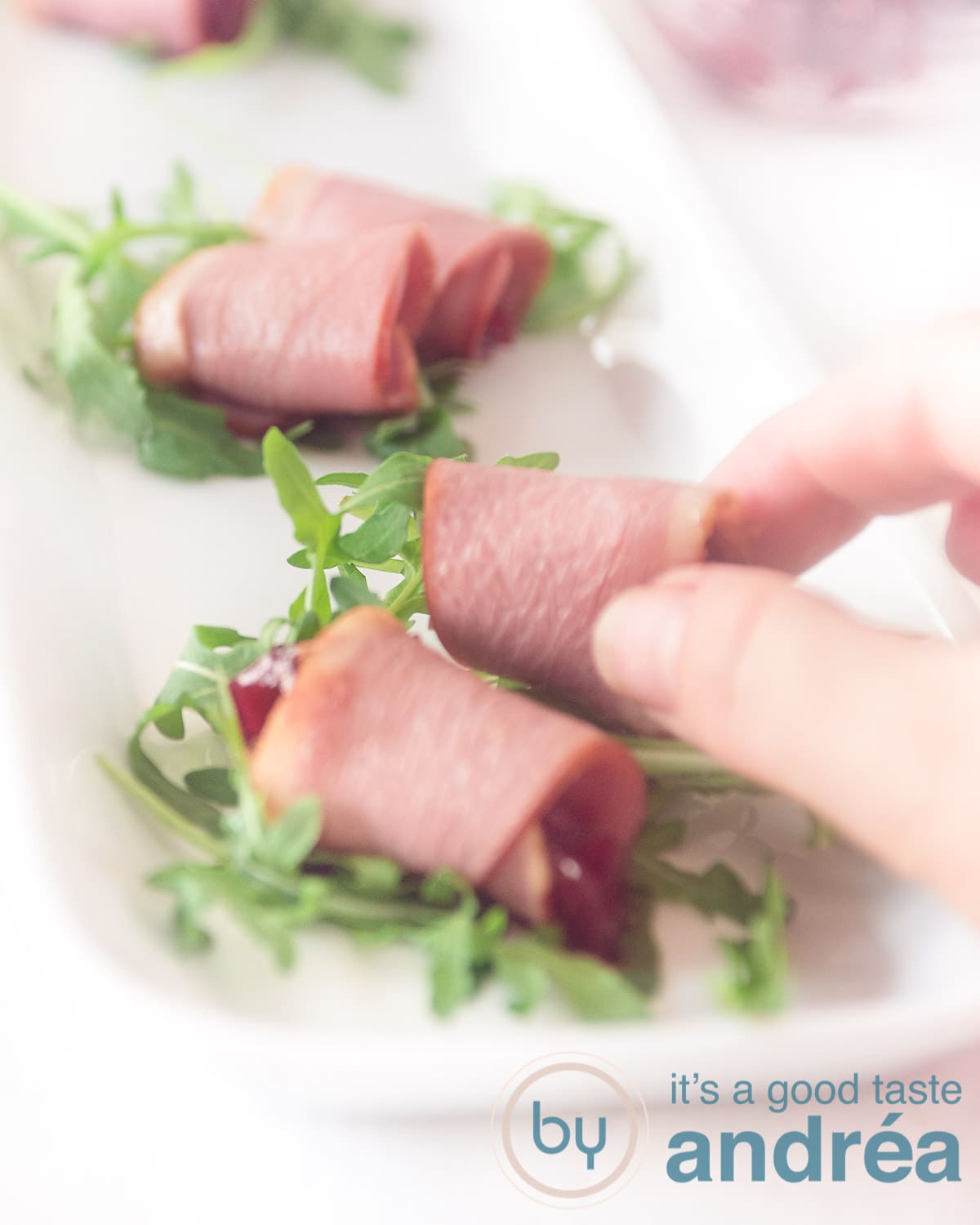 Een hand pakt een rolletje met eendenborst gevuld met cranberry compote en rucola