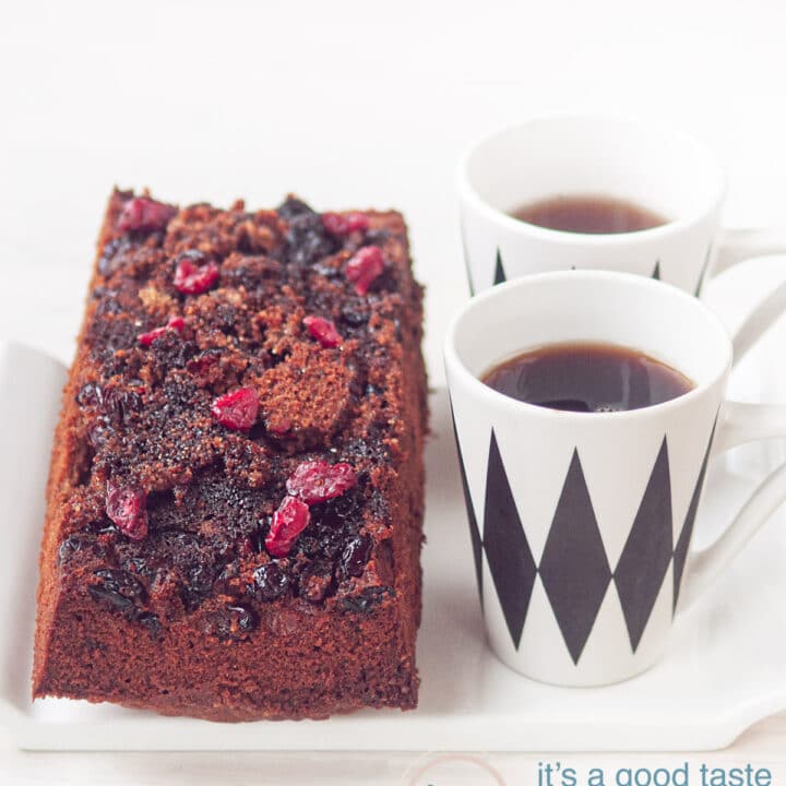 Op een wit schaaltje ligt een cake met cranberry topping en twee kopjes met koffie