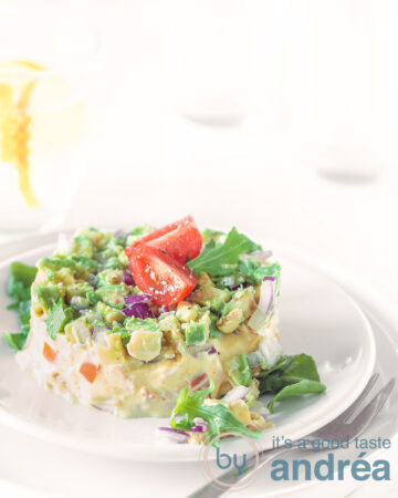 Smoked chicken and avocado salad formed into a tower, placed on a white plate that's on a second white plate. On a white background