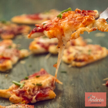 Een mini kerstpizza met smeltende kaas wordt met een vork opgetild boven de andere pizza's