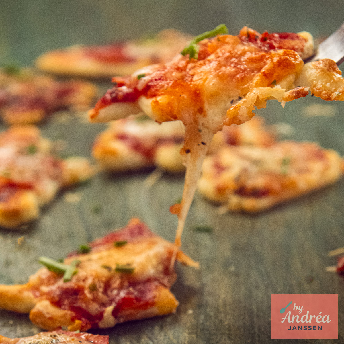 Een mini kerstpizza met smeltende kaas wordt met een vork opgetild boven de andere pizza's