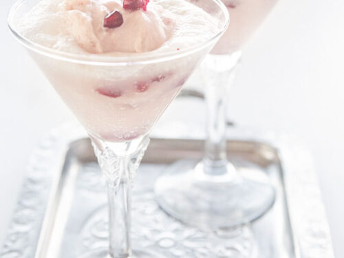 Twee glazen met een spoom van granaatappel yoghurt ijs met prosecco en verse granaatappel pitjes