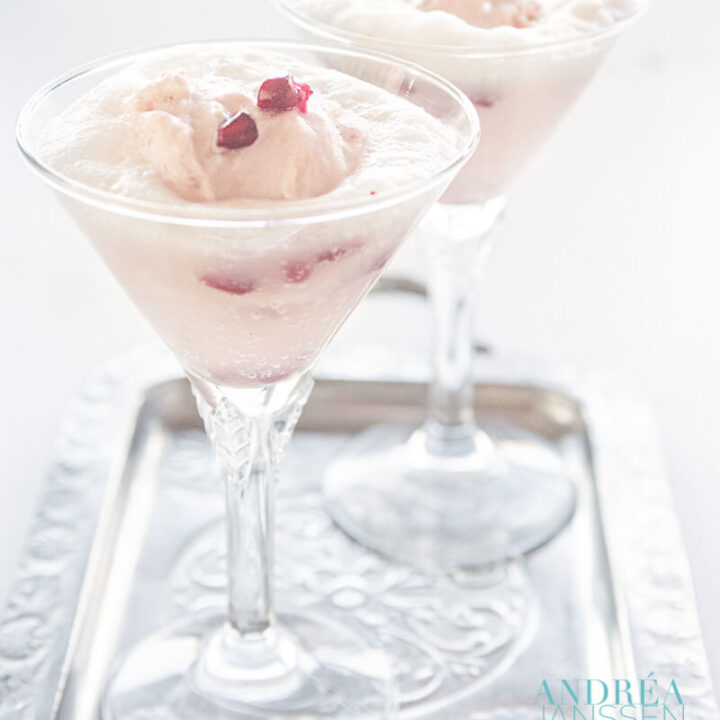 Twee glazen met een spoom van granaatappel yoghurt ijs met prosecco en verse granaatappel pitjes