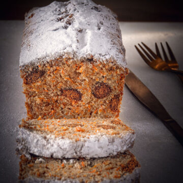 Wortelcake met pepernoten op een betonnen ondergrond. Een plakje is afgesneden