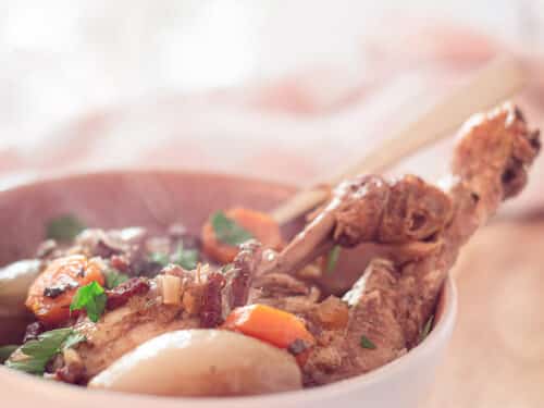 Coq au vin in a white pan on a wooden table