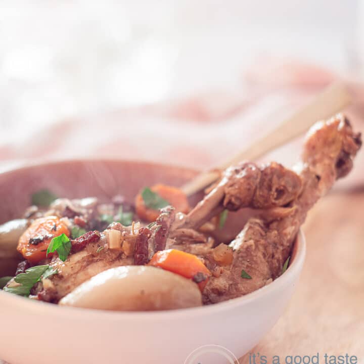 Coq au vin in a white pan on a wooden table