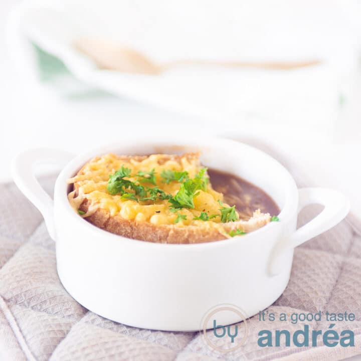 Een witte soepkom gevuld met rode uiensoep en een stukje gegratineerd stokbrood