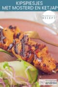 Twee gegrilde kipspiesen op een roze bord met een komkommersalade erbij. Een tekst bovenin: makkelijk recept, kipspiesjes met mosterd en ketjap
