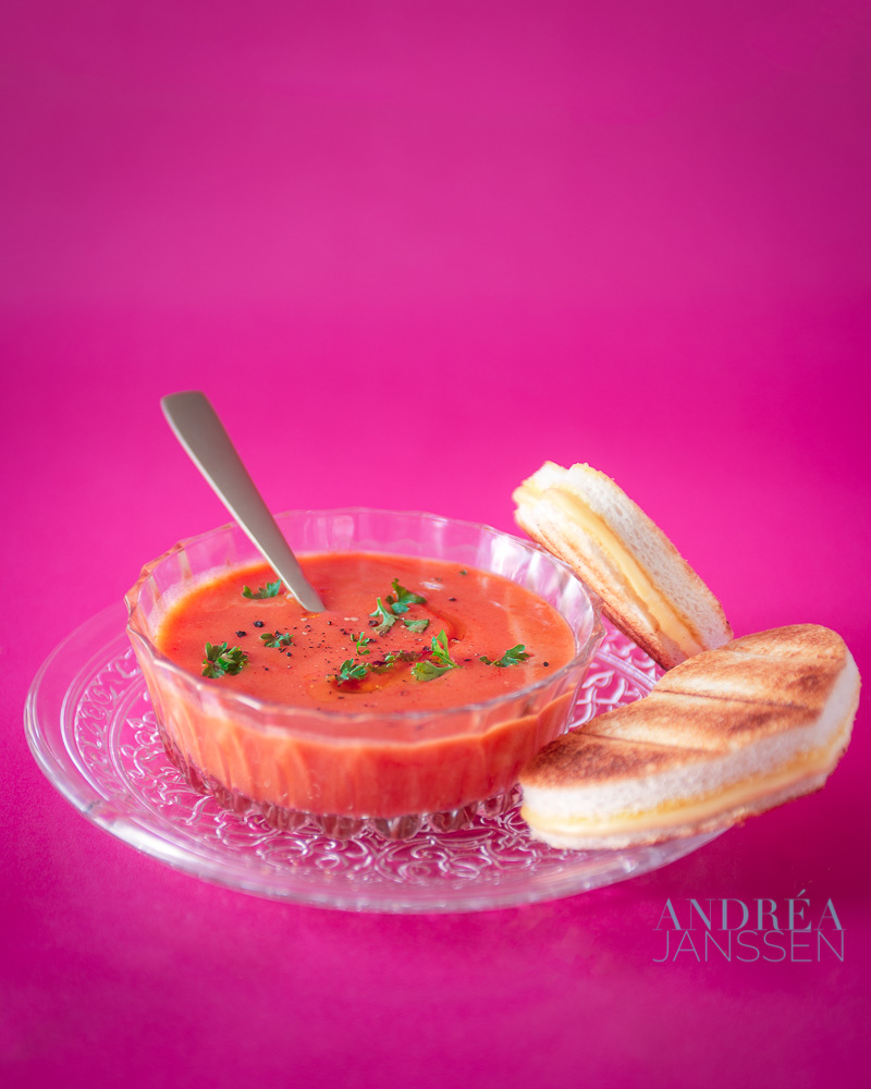 een glazen kom met tomatensoep, hartjes tosti op een roze achtergrond