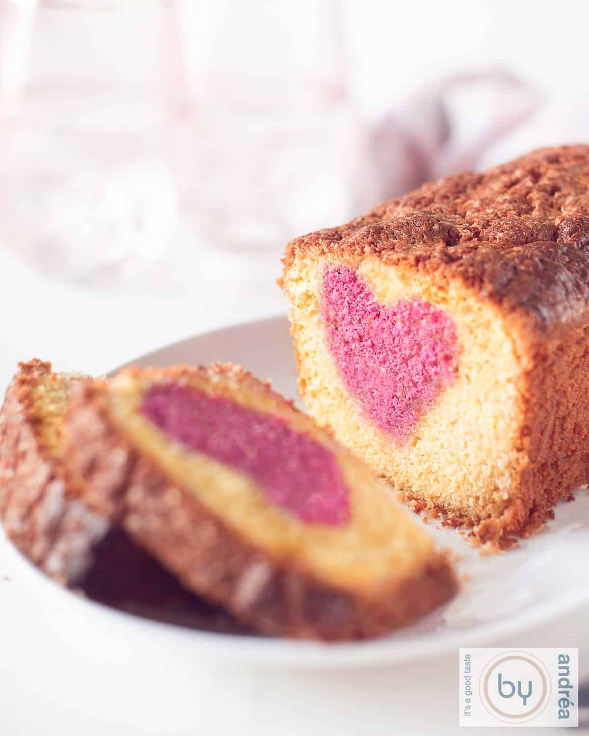 Een hoogtefoto met een witte schaal met daarop een cake waar twee plakjes afgesneden zijn. Een roze hart is zichtbaar