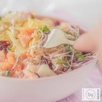 Een vierkante foto met spaghetti, gerookte zalm en Parmezaanse kaas. Een vork prikt erin.
