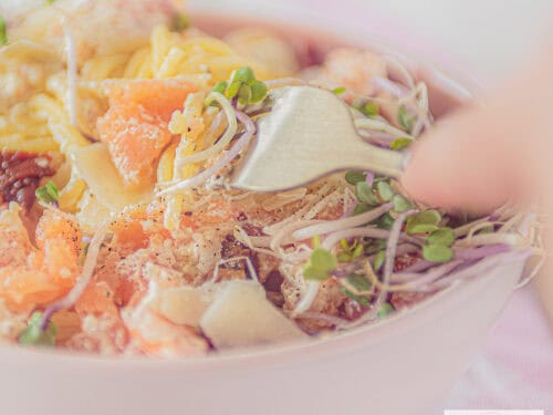 Een vierkante foto met spaghetti, gerookte zalm en Parmezaanse kaas. Een vork prikt erin.
