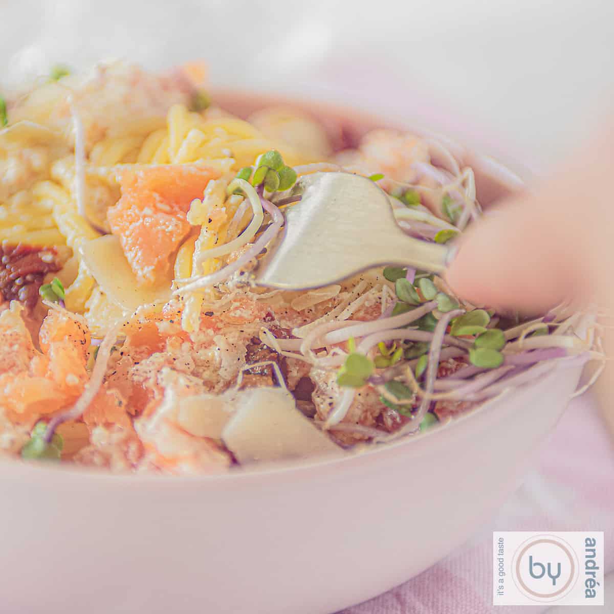 Een vierkante foto met spaghetti, gerookte zalm en Parmezaanse kaas. Een vork prikt erin.