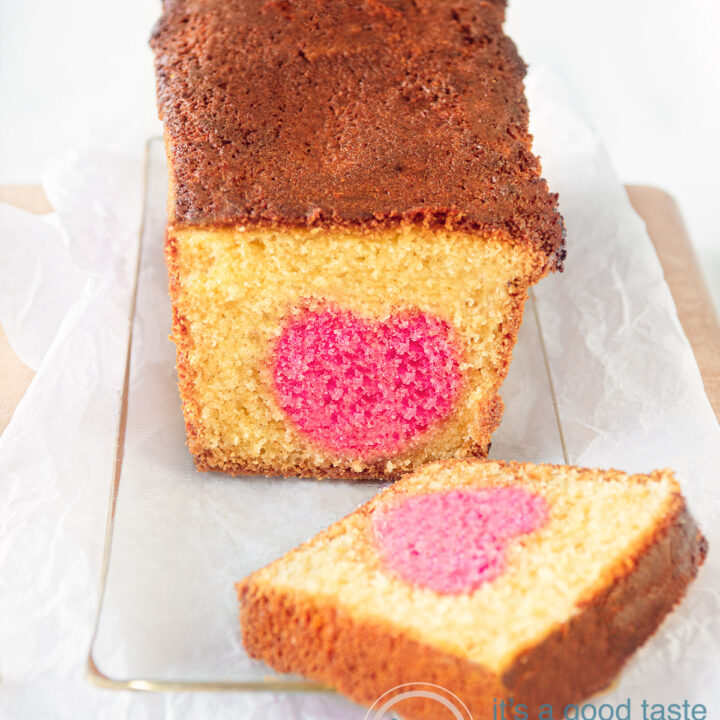 Een glazen schaal met een cake met een roze hartje. Een plakje afgesneden