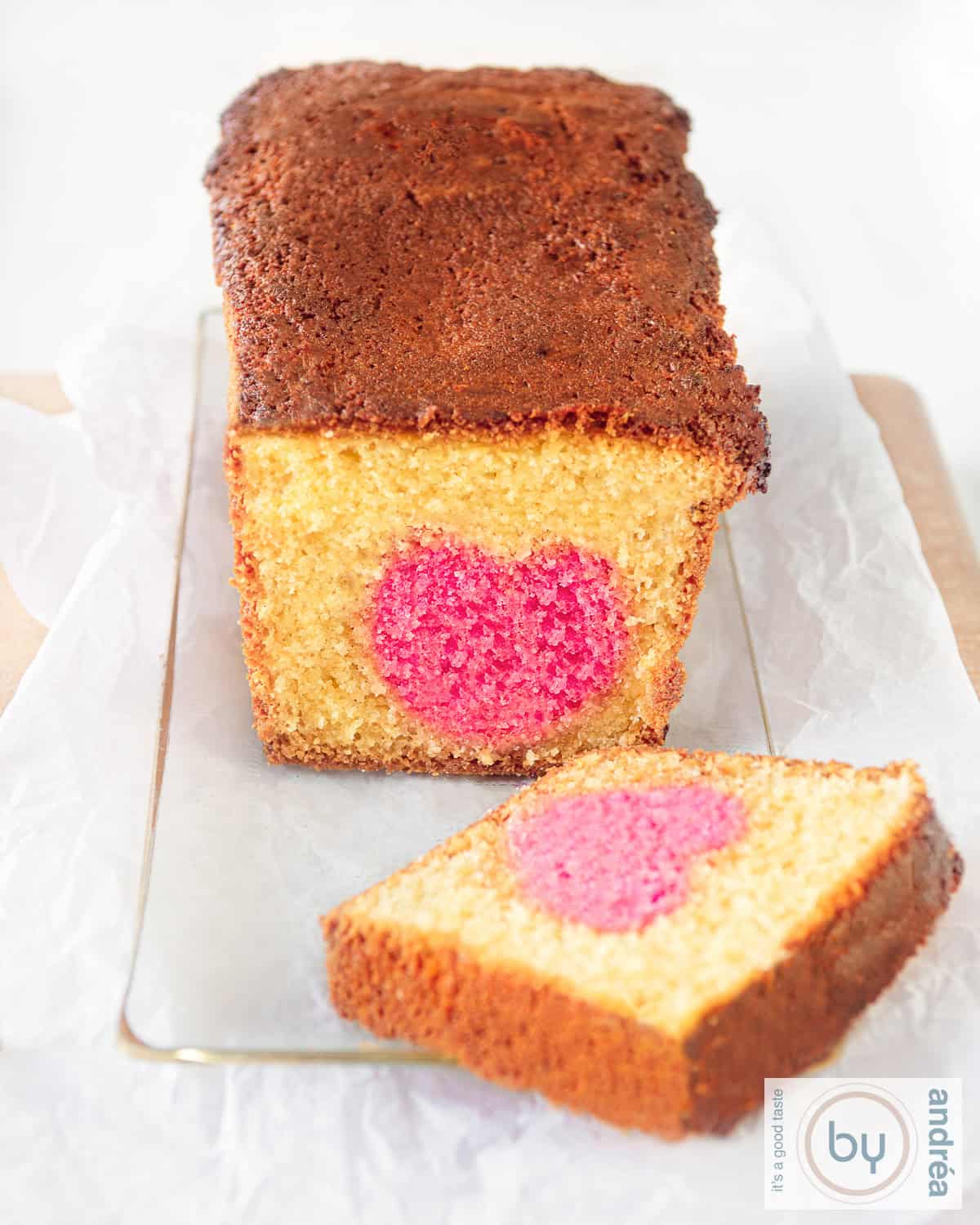 Een hoogtefoto van een cake op een glazen cakeschaal waar een plakje is afgesneden. Een roze hart is nu zichtbaar.