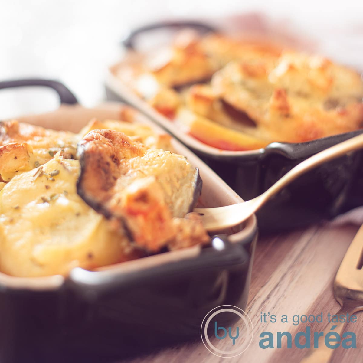 Een vierkante foto met twee individuele ovenschaaltjes gevuld met Griekse moussaka op een houten plank