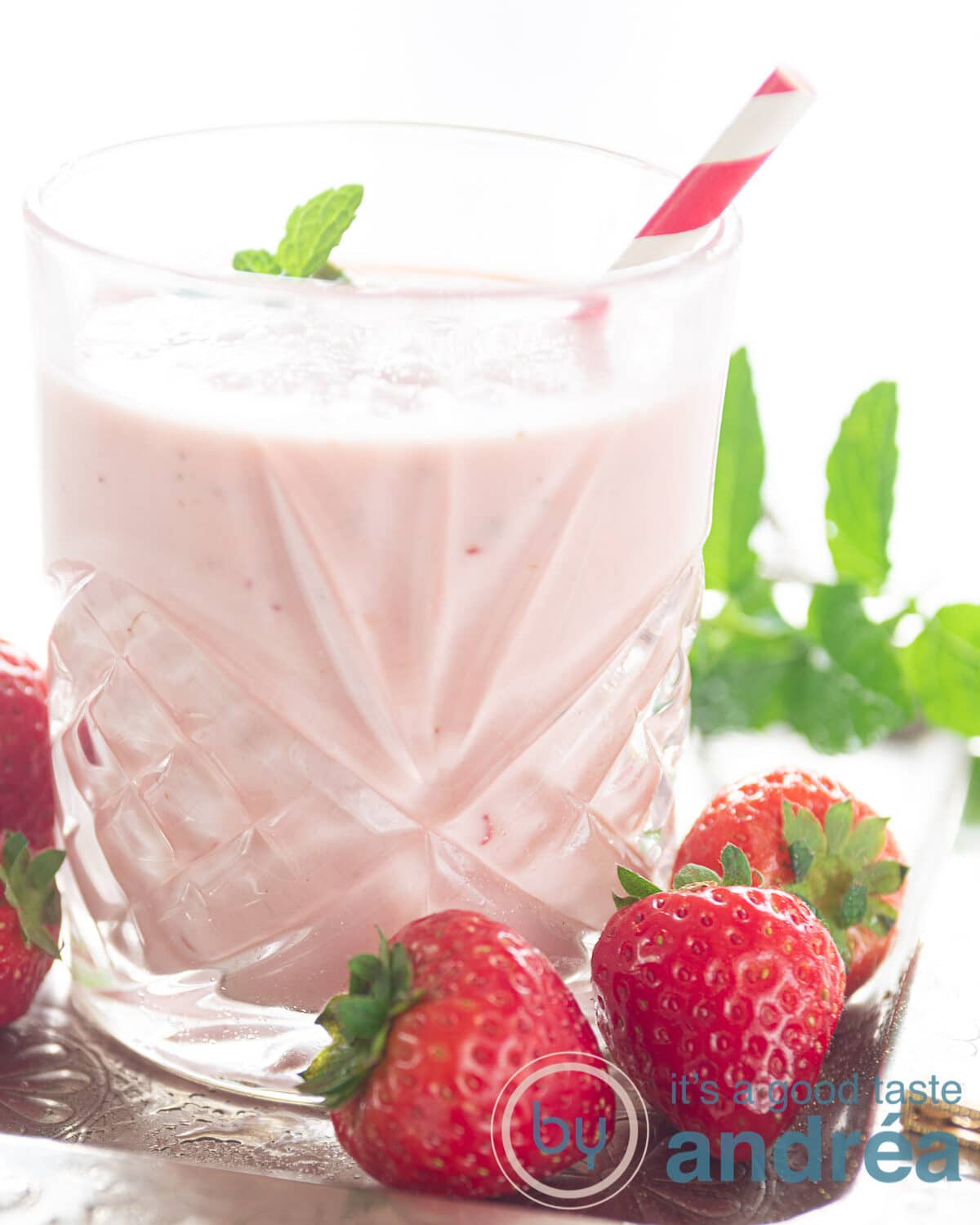 Een glas gevuld met een aardbeien smoothie met sinaasappel. Munt in de achtergrond, losse aardbeien in de voorgrond