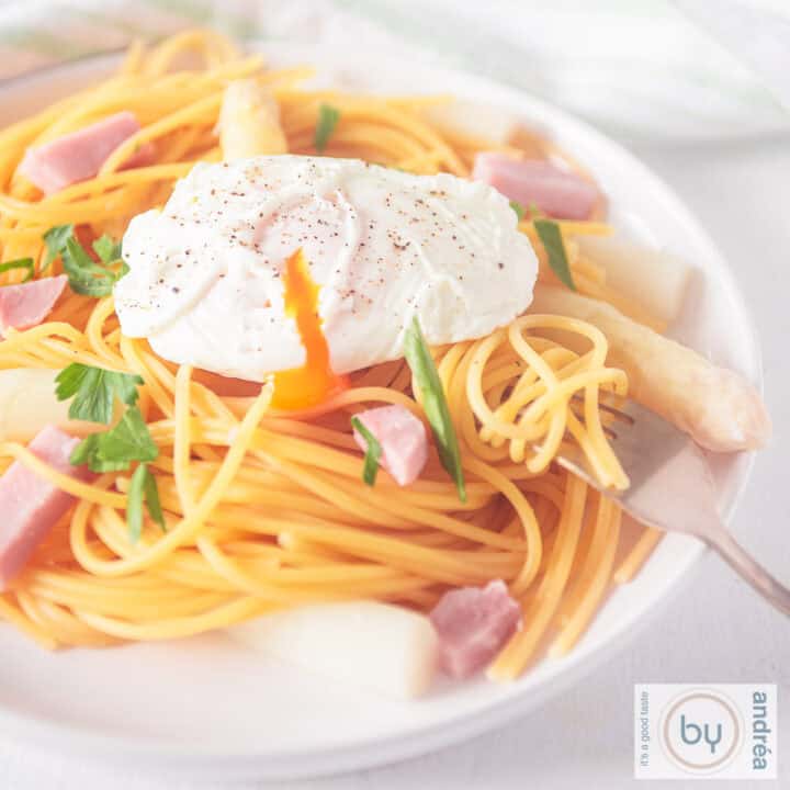 A square picture of a white plate with spaghetti, ham asparagus and poached egg.