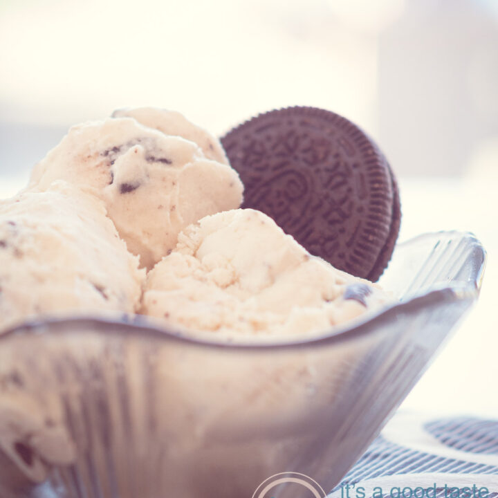 Een macroopname van een zwart glazen schaaltje op een zwart wit geblokt servet gevuld met drie bollen Oreo ijs en een koekje er ingestoken