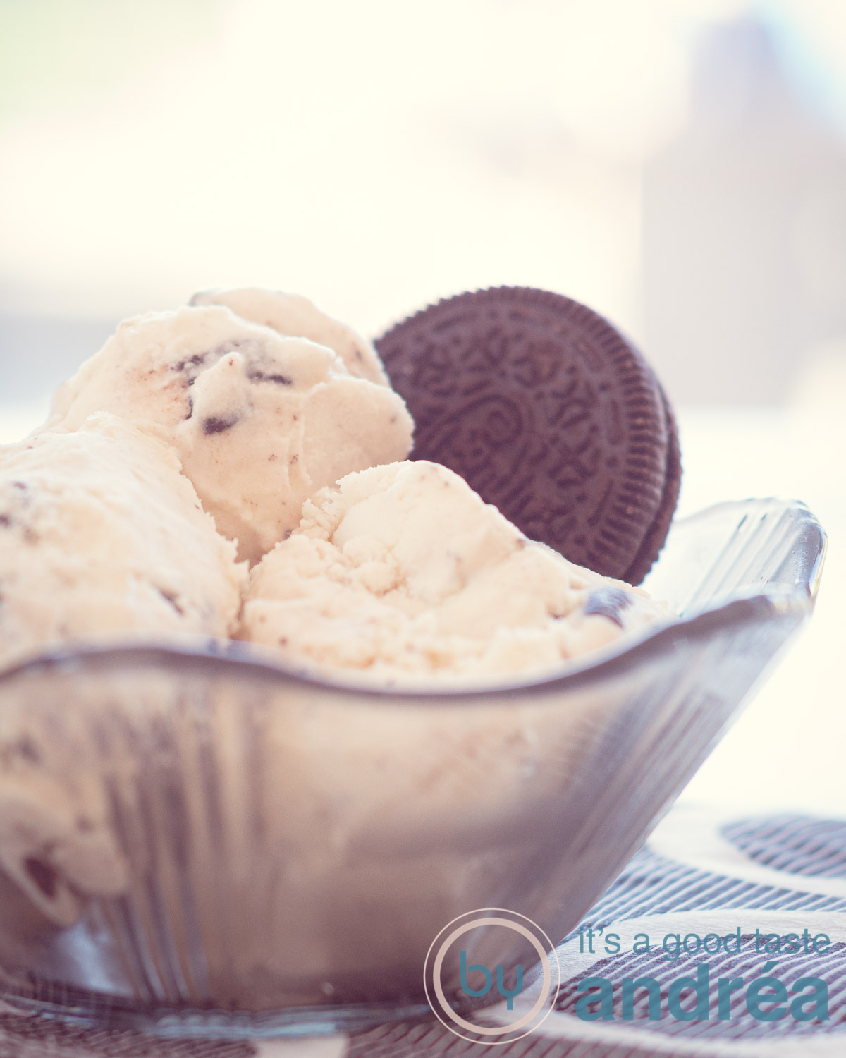 Een macroopname van een zwart glazen schaaltje op een zwart wit geblokt servet gevuld met drie bollen Oreo ijs en een koekje er ingestoken