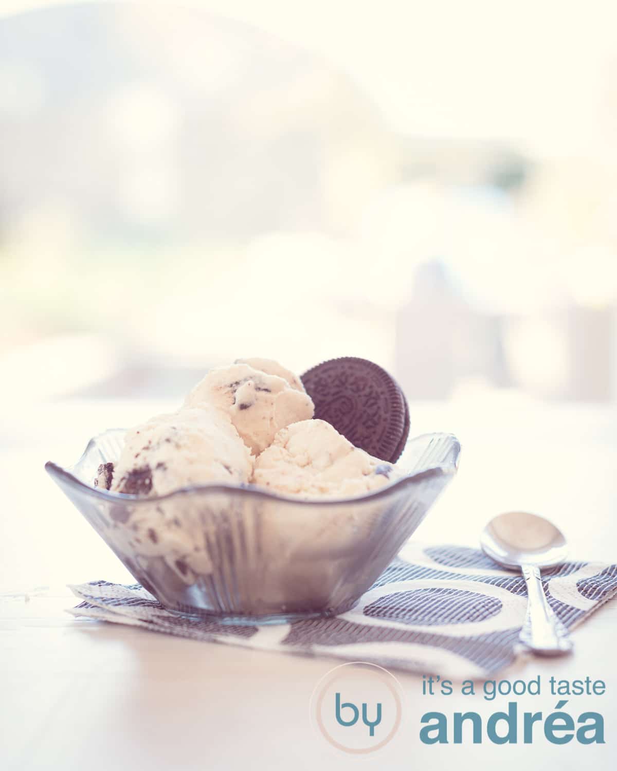 Een zwart glas schaaltje gevuld met drie bollen Oreo ijs en een koekje op een witte ondergrond met een zwart wit servet.