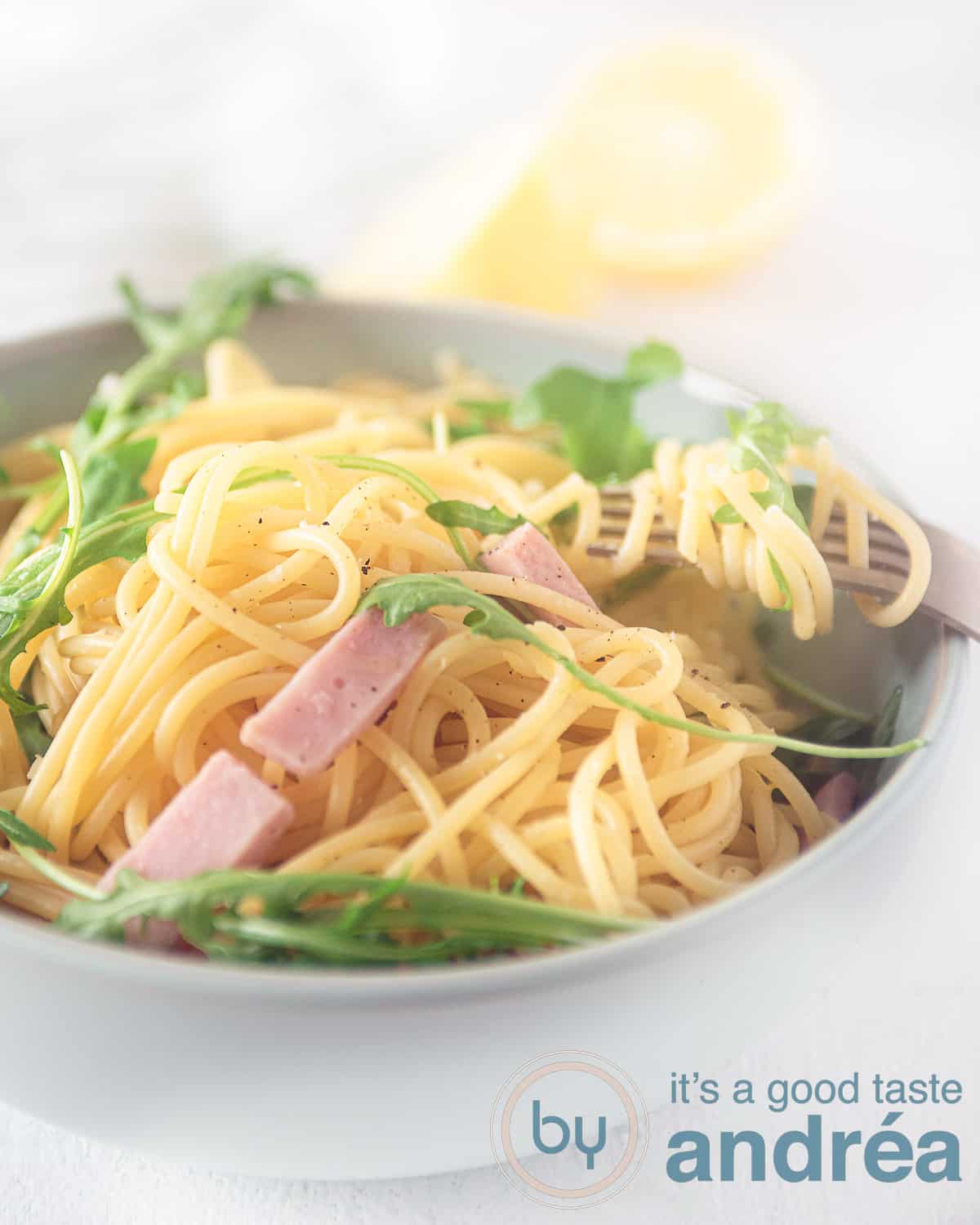a gray bowl with spaghetti, ham and arugula on a white background