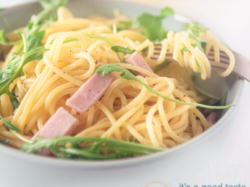 Een vierkante fotonet een grijze schaal gevuld met ham, rucola en spaghetti op een witte ondergrond