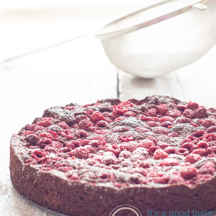 Een witte plank met een frambozen brownie cake bestrooit met poedersuiker