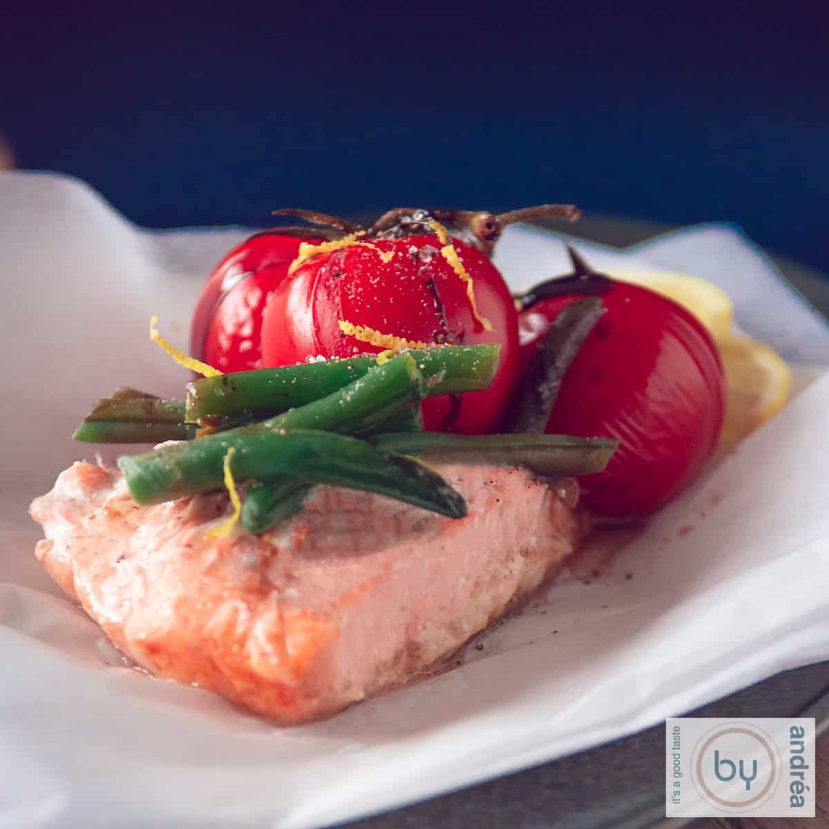 Een vierkante foto van een bakpapier met een zalm met daarop boontjes, gestoofde tomaten en citroenrasp.