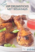 een drumstick in het midden en een aantal aan de linkerzijde ernaast. Een glazen schaaltje met chilisaus rechts. Een tekstoverlay: Kip drumsticks met sojasaus, avondeten, makkelijk recept.