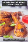 Close-up van drie kipdrumsticks met een glanzende donkere ketjapsaus op een wit bord, bestrooid met ringetjes lente-ui, met een glazen schaaltje rode chilisaus ernaast