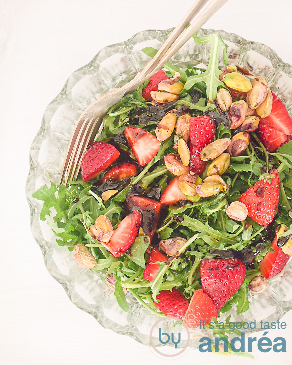 Een foto van bovenaf van een glazen schaal gevuld met aardbeien salade en pistache noten