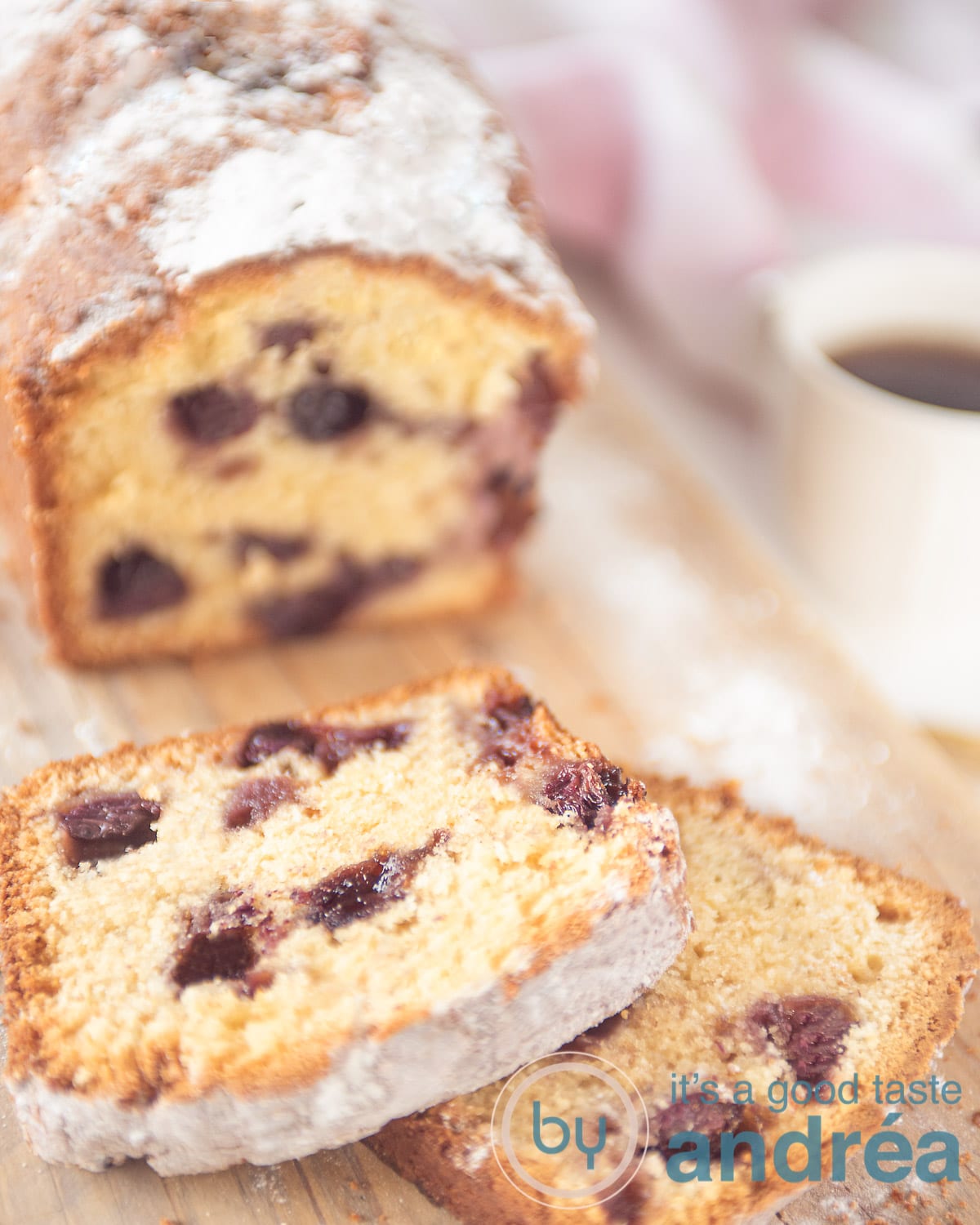 Een houten plank met een cake met blauwe bessen. Twee plakjes eraf. Aan de rechterkant een kopje koffie