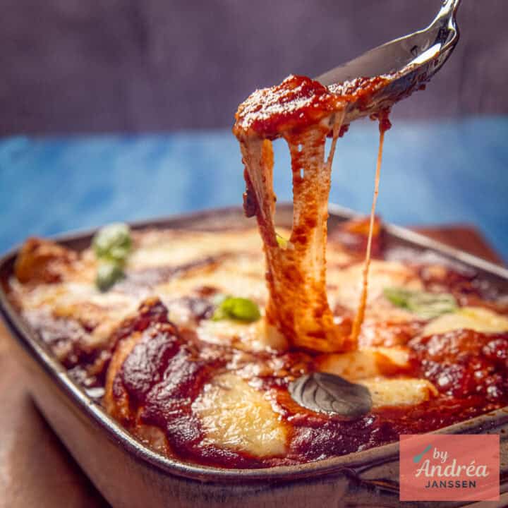 Kip pizzaiola met tomatensaus en draderige mozzarella wordt met een vork uit de ovenschaal gehaald.