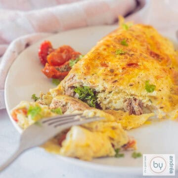 Een vierkante foto met een gevulde omelet met tonijn op een wit bord