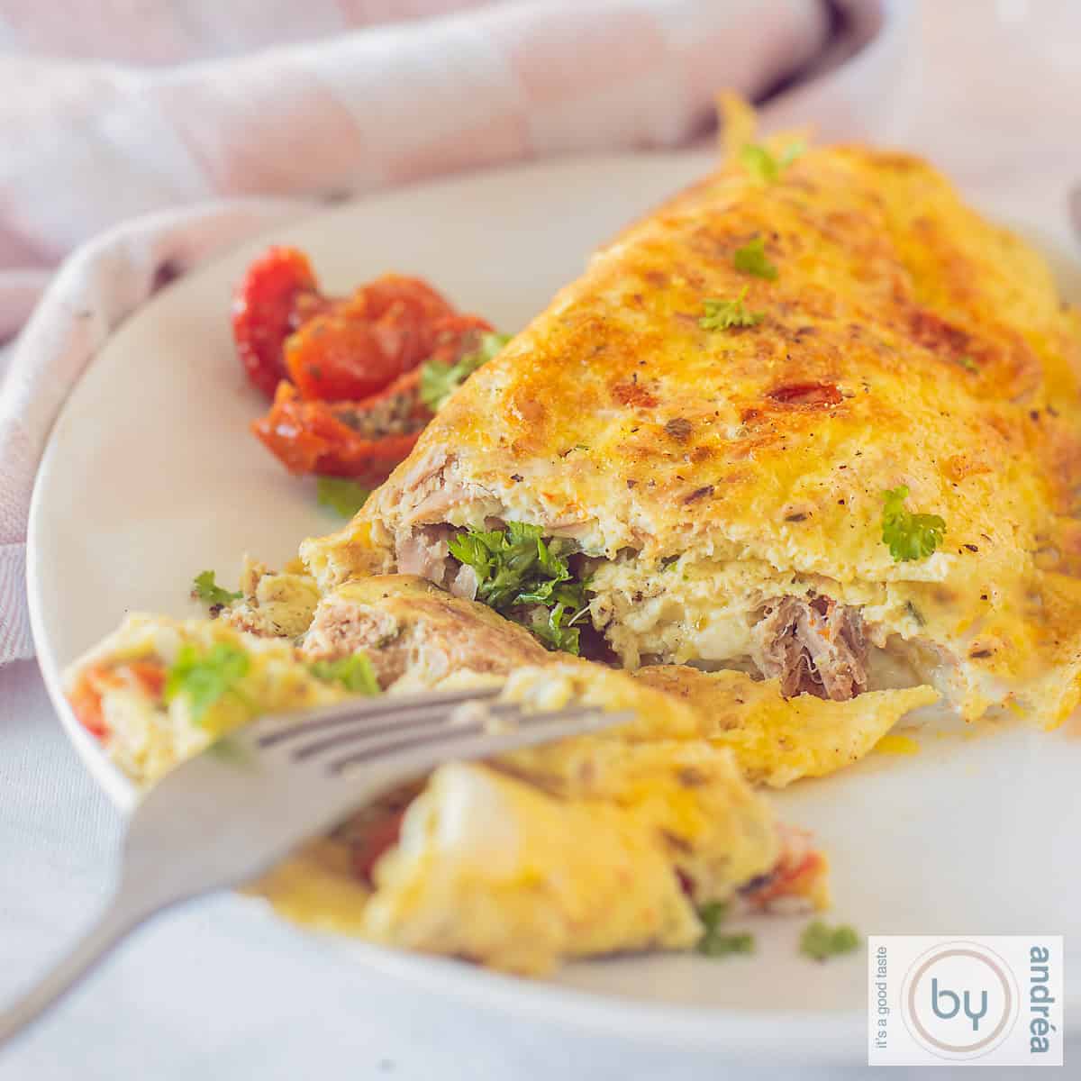 Een vierkante foto met een gevulde omelet met tonijn op een wit bord