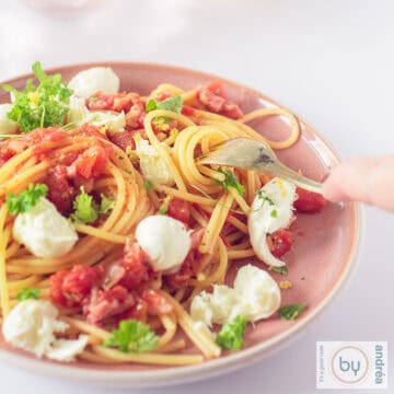 Een vierkante foto van een roze bord gevuld met spaghetti, bacon, tomaten, mozzarella en peterselie