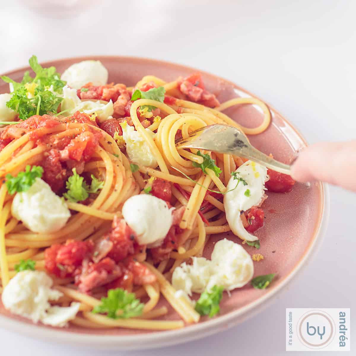 Een vierkante foto van een roze bord gevuld met spaghetti, bacon, tomaten, mozzarella en peterselie