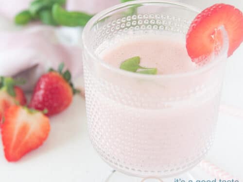 een vierkante foto met een glas met aardbeiensmoothie. Gegarneerd met aardbeien en basilicum